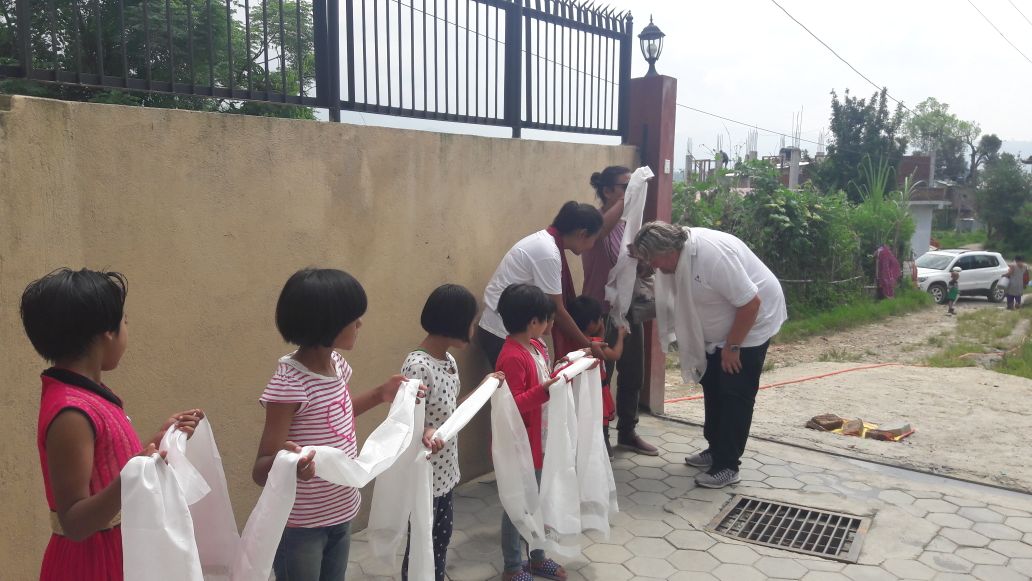 Anak-anak menyambut pengunjung dengan syal putih di luar ruangan