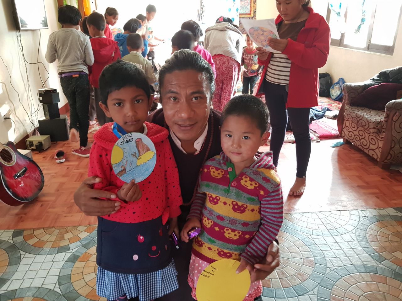 Orang dewasa bersama dua anak yang memegang karya seni di dalam ruangan